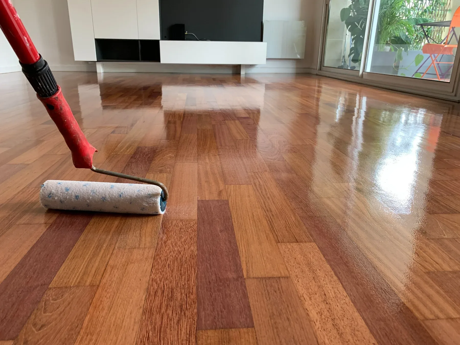 Application d’une finition au rouleau sur un parquet en lames.