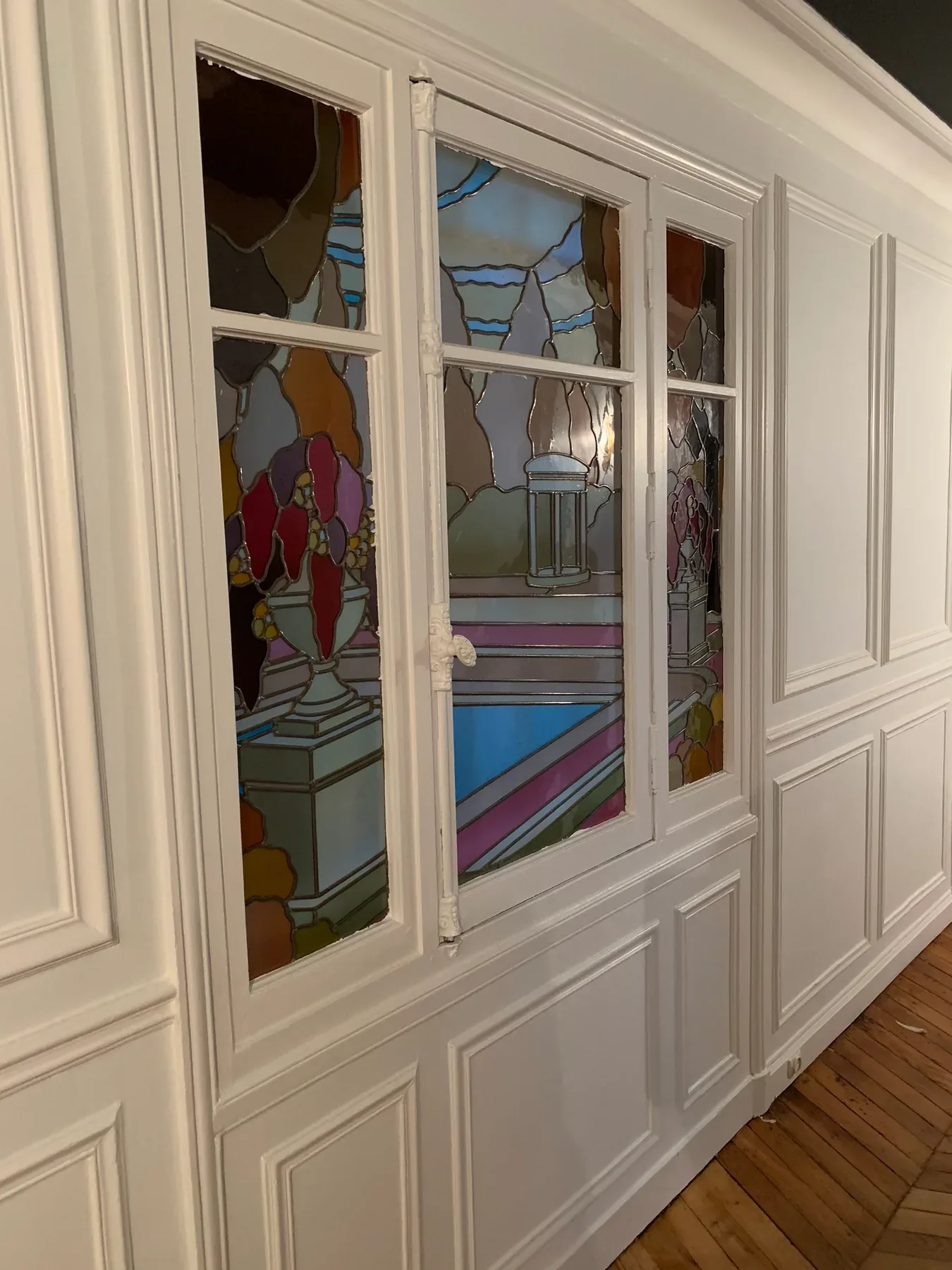 Boiseries blanches encadrant un vitrage décoratif coloré.