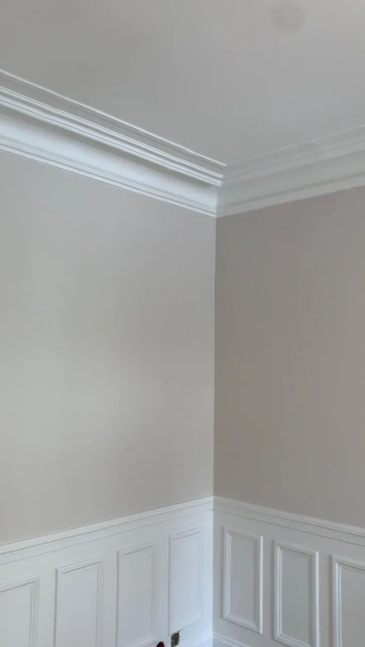 Détail de murs clairs, de moulures et de boiseries blanches.