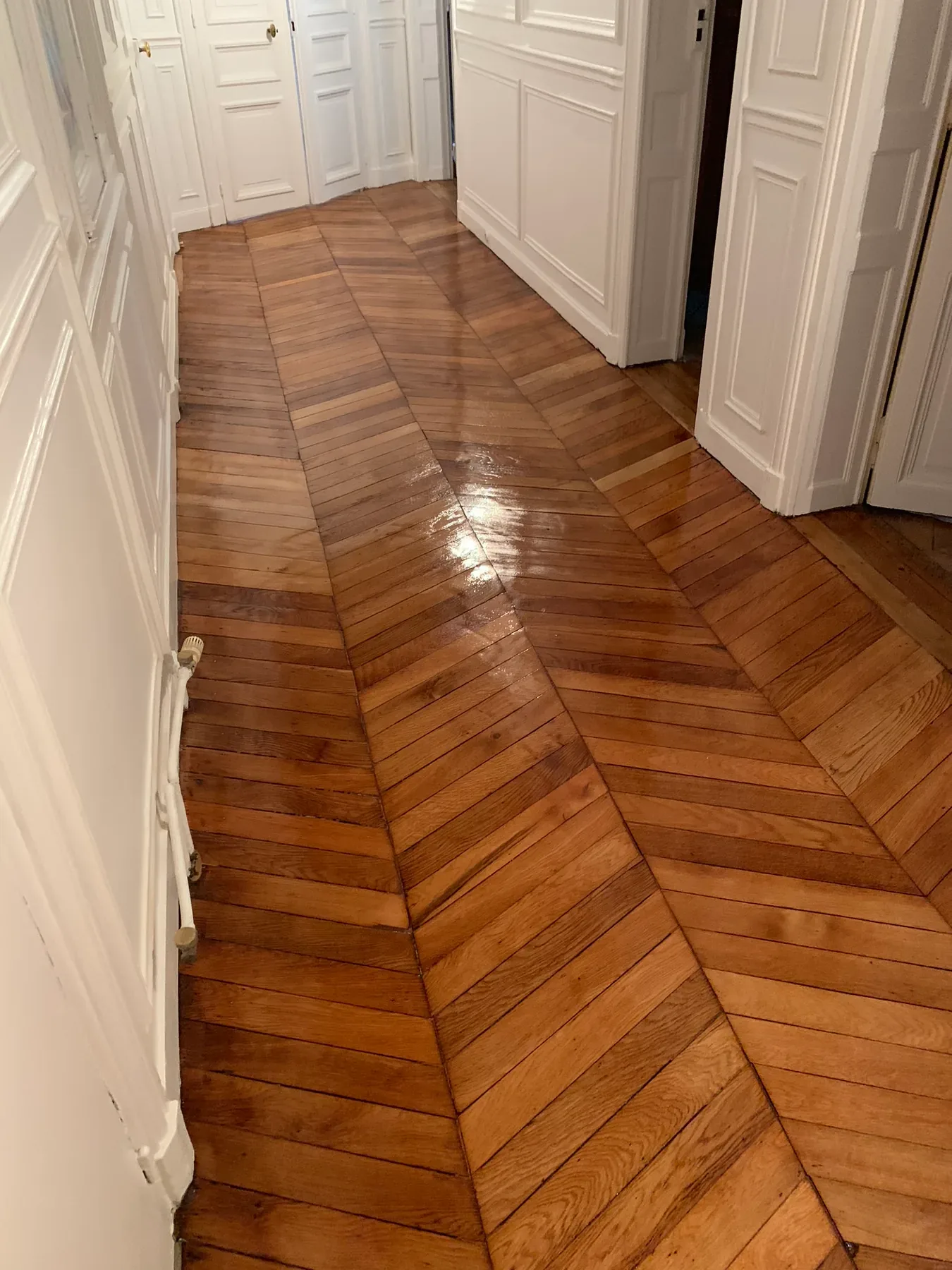 Même couloir avec un parquet en chevrons plus foncé et brillant après rénovation.