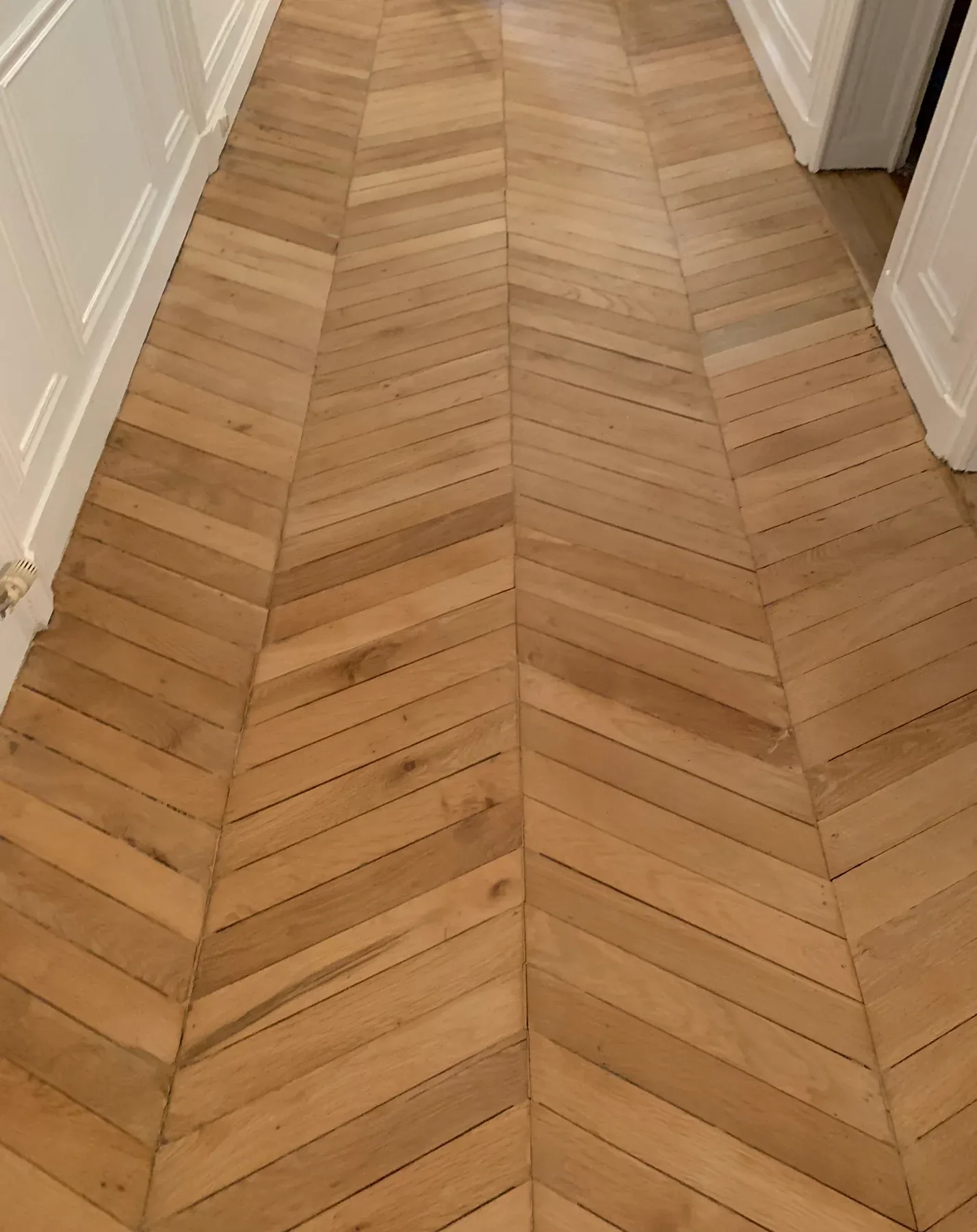 Parquet en chevrons clair et mat dans un couloir, avant rénovation.