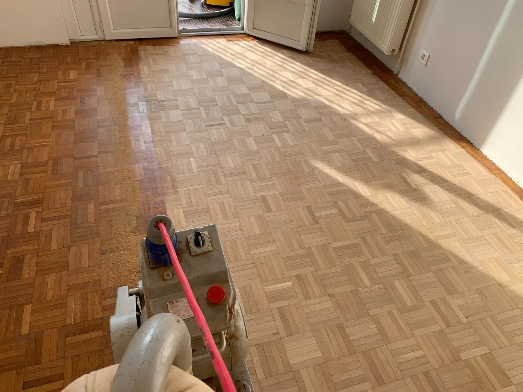 Ponçage en cours d’un parquet mosaïque avec une ponceuse de sol.