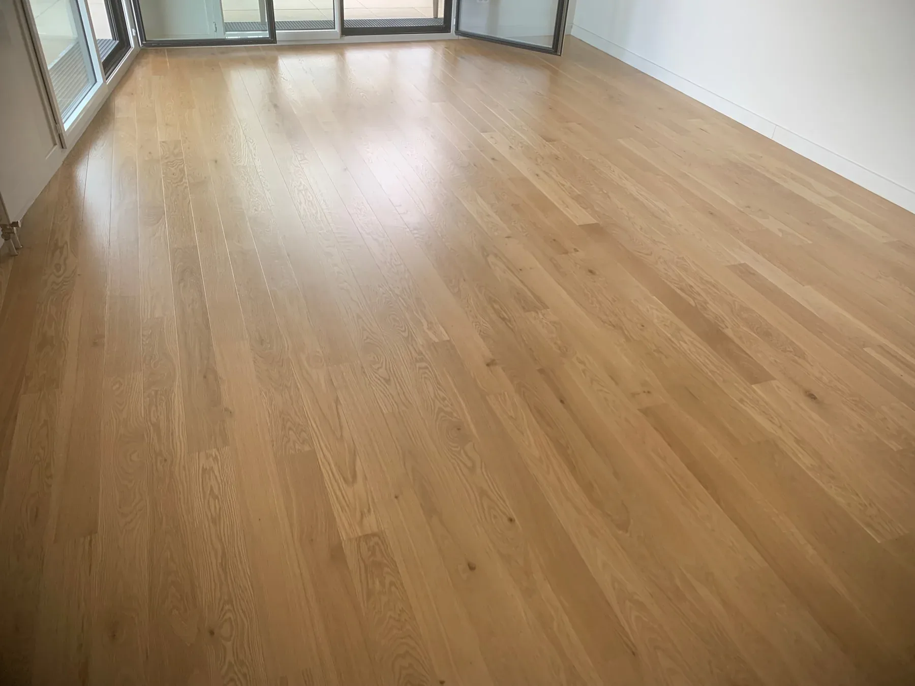 Vue du parquet en lames larges et des plinthes près d’une baie vitrée.